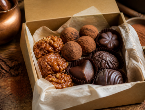 Open gift box filled with assorted chocolate truffles, caramel clusters, and molded chocolates.