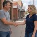 Two people in t-shirts and jeans shaking hands on a small-town sidewalk