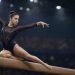 Gymnast in a navy sequined leotard balancing on a beam under arena lights