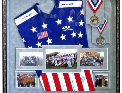 Shadow box display with a blue cycling jersey, medals, race photographs, and an American flag.