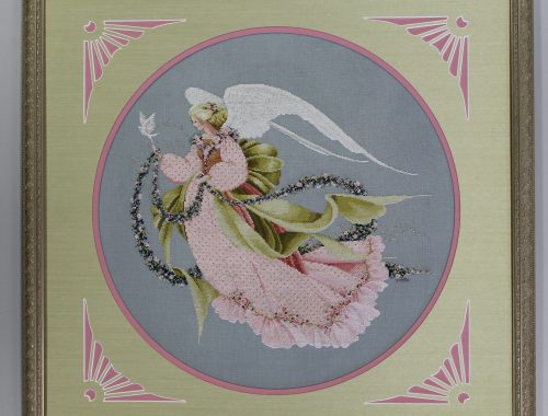 Framed round embroidery showing a delicate angel with pink wings and flowers on a pale blue background.