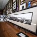 Interior of a custom frame shop with a framed 1908 Prescott panoramic photograph on the counter, surrounded by framed artwork and molding samples.