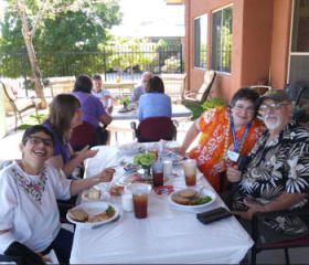 Older adults sit together at a patio table sharing a meal at the day center.